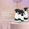 A group of KALA room fragrance spray bottles are displayed on a pink pedestal in front of a blurred background of a decorated event space with chandeliers and string lights. Produktbild-Vorschau
