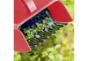 A close-up of a red berry picker scooping blueberries from a bush. Anteprima dell’immagine prodotto