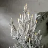 A close-up of a flocked Christmas tree decorated with candle-shaped LED lights. Produktbild-Vorschau