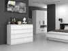 A modern bedroom with a white dresser, a large white wardrobe, and a bed. The dresser is in the foreground, with decorative items on top. The wardrobe is in the midground, and the bed is in the background. Produktbild-Vorschau