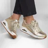A pair of gold Skechers sneakers on a person's feet. Voir les images du produit
