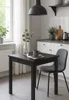A small black dining table with a gray chair and a mug on it, set in a bright kitchen with a window and cabinets. Produktbild-Vorschau