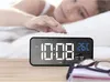 A person reaching for a digital alarm clock on a bedside table. Podgląd zdjęcia produktu