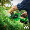 A person is using a green electric hedge trimmer to trim a bush. Podgląd zdjęcia produktu