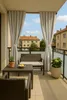 A balcony furnished with outdoor seating and a small table, overlooking buildings and a blue sky with clouds. Anteprima dell’immagine prodotto