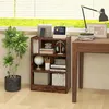 A bookshelf with various items on it, placed next to a desk and a plant, near a window. Produktbild-Vorschau
