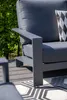 A close-up view of an outdoor lounge chair's armrest and cushion, with greenery in the background and a patterned rug in the foreground. Produktbild-Vorschau