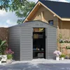 A grey storage shed is shown outdoors in a backyard setting, with a wooden house and fence in the background. Plants and flowers are visible in pots around the shed. Produktbild-Vorschau