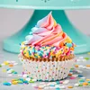 A colorful cupcake with rainbow frosting and sprinkles sits on a table in front of a teal cake stand. Náhled obrázku produktu