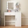 A white vanity table with a lighted mirror and shelves, displaying makeup and accessories. Náhled obrázku produktu