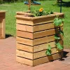 A wooden planter box filled with plants sits on a brick patio next to a grassy area. Produktbild-Vorschau