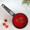 A top-down view of a saucepan filled with red sauce, garnished with herbs, and surrounded by cherry tomatoes on a light gray surface. Produktbild-Vorschau