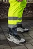 A person wearing high-visibility work pants and shoes, standing on a paved surface. Produktbild-Vorschau