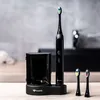 A black electric toothbrush and its accessories are displayed on a wooden surface with a blurred background. Náhled obrázku produktu