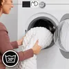 A woman is putting a white blanket into a washing machine. A laundry symbol indicating 30 degrees Celsius is visible in the bottom left corner. Náhled obrázku produktu