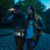 Two people are hiking at night, one is holding a flashlight and the other has a headlamp on. Produktbild-Vorschau