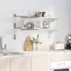 A kitchen scene with a wall-mounted shelf unit holding jars and a mug, above a countertop with a sink, cutting boards, a vase of greenery, a toaster, and a coffee machine. Produktbild-Vorschau