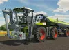 A large agricultural machine, likely a self-propelled sprayer or slurry tanker, is shown in a field under a partly cloudy sky. Náhled obrázku produktu