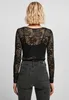 A woman wearing a black lace long-sleeved top and grey jeans, viewed from the back. Produktbild-Vorschau