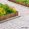 A wooden border is used to edge a garden bed with plants, separating it from a paved walkway. Voir les images du produit