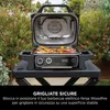 An open electric grill with food cooking on it, placed outdoors on a stand, with greenery in the background. Náhľad obrázku produktu