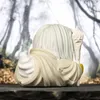 A close-up view of a stylized figurine from behind, set against a blurred background of trees. Podgląd zdjęcia produktu
