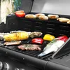 A close-up shot of a black gas grill with various foods cooking on it, including sausages, corn on the cob, peppers, steak, and fish. Produktbild-Vorschau