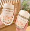 Two glass water bottles with floral designs and pearl handles are held up against a blurred background of shelves and plants. Podgląd zdjęcia produktu