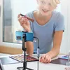 A young woman is filming herself applying makeup using her smartphone, which is mounted on a tripod and connected to a capture card. Náhled obrázku produktu