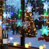 Christmas lights in the shape of snowflakes hanging in a window with a Christmas tree in the background. Produktbild-Vorschau
