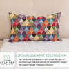 A rectangular pillow with a geometric triangle pattern is placed on a white fluffy rug, which is on a light-colored sofa. Produktbild-Vorschau