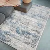 A rug is placed on the floor next to a sofa and a pouf. Podgląd zdjęcia produktu