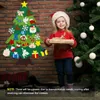 A young girl in a Santa hat holds a gift next to a felt Christmas tree and a real Christmas tree. Produktbild-Vorschau
