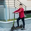 A young boy is standing on a scooter on a paved walkway outside a building. Náhľad obrázku produktu