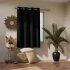 A black blackout curtain is shown hanging on a window rod in a room with decorative items. Produktbild-Vorschau