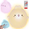 Three cute, cartoon-like bunny-shaped night lights in pink, yellow, and blue are displayed. A remote control is shown in the upper right corner. Produktbild-Vorschau