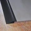 A close-up view of a black PVC threshold profile installed between a wooden floor and a gray surface, likely a tile or linoleum floor. Podgląd zdjęcia produktu