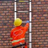 A person wearing safety gear is climbing a ladder against a brick wall. Produktbild-Vorschau