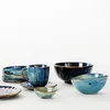 A collection of ceramic tableware, including bowls, plates, and a mug, arranged on a white surface. Produktbild-Vorschau