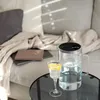 A glass water pitcher and a glass of water with lemon slices are placed on a coffee table in front of a couch. Anteprima dell’immagine prodotto