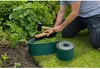 A person is installing a garden border. The border is green and flexible, and the person is using a mallet and a piece of wood to help push it into the ground. Produktbild-Vorschau