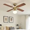 A ceiling fan with wooden blades and a brass finish is mounted on a white, paneled ceiling above a bed. Náhľad obrázku produktu