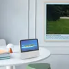 A white smart speaker with a screen displaying a tropical island is placed on a white table next to a stack of books and a small lamp. Náhľad obrázku produktu