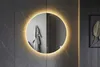 A round, frameless mirror with LED lighting is mounted on a dark gray tiled wall. A gray towel is hanging on the wall reflected in the mirror. Anteprima dell’immagine prodotto