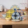 A collection of colorful, patterned ceramic dishes and mugs arranged on a wooden table. Náhled obrázku produktu