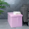 A pink storage ottoman sits on a tiled floor next to a gray sofa, with a plant in the background. Náhled obrázku produktu