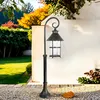A black outdoor lantern on a post in a garden setting with autumn foliage. Produktbild-Vorschau