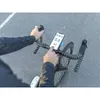 A person's hands are shown operating a smartphone mounted on a bicycle handlebar. The phone displays a timer and speed readings. Náhled obrázku produktu