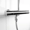 A close-up shot of a chrome shower mixer tap mounted on a white tiled wall, with a grey shower hose attached. Produktbild-Vorschau