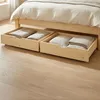 Underneath a bed frame, two open wooden drawers are visible, each containing folded blankets or linens. Voir les images du produit
